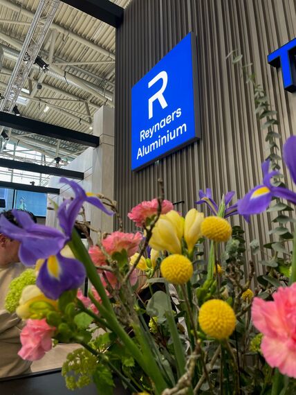 The Reynaers Aluminium logo behind flowers.