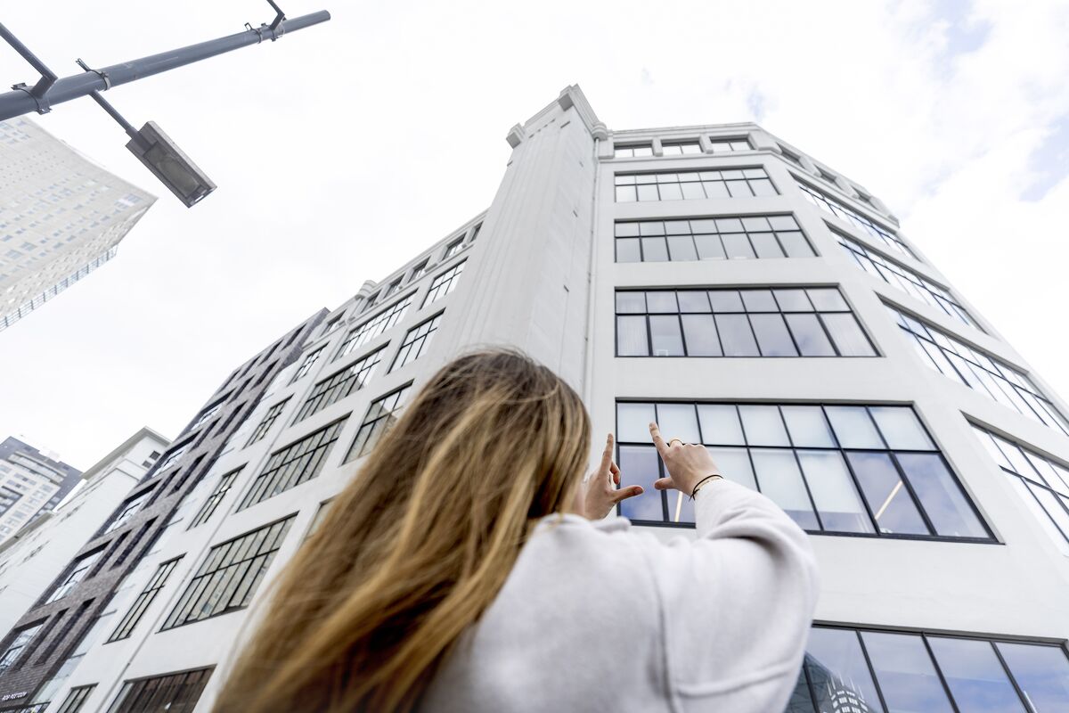 Woman holding up her hands towards a white mid-rise building with lots of windows.