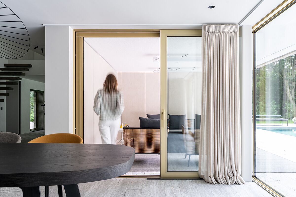 Woman entering modern villa through golden sliding doors.