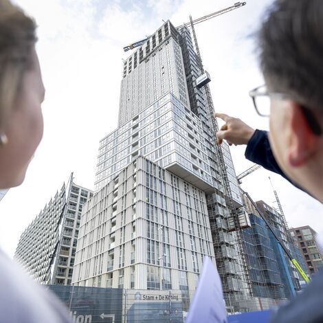 Man and woman pointing at grey high-rise project under construction.