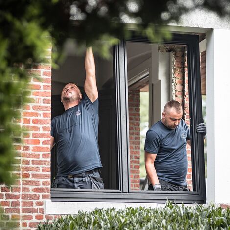 Two men installing black aluminium window in private renovation.