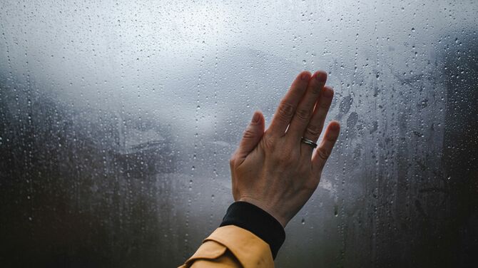 Woman wiping moist window pane with bare hand.