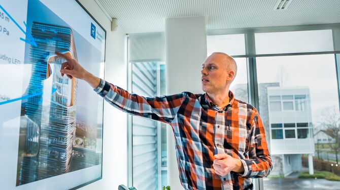 Un homme blanc en chemise à carreaux pointant vers un écran de présentation.