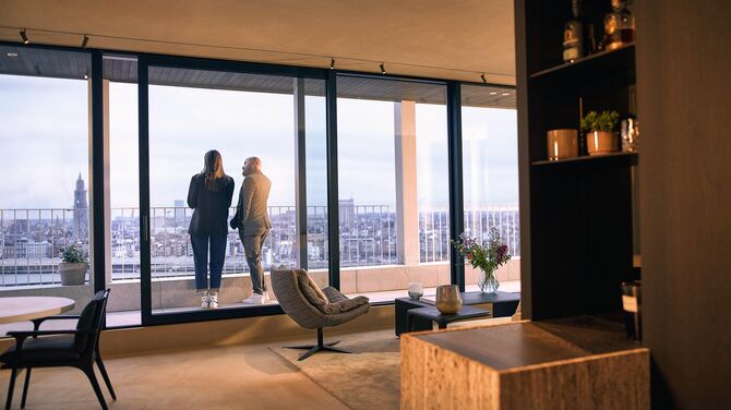 Alt : Vue intérieure d'un appartement moderne avec de larges portes coulissantes et deux personnes sur un balcon.