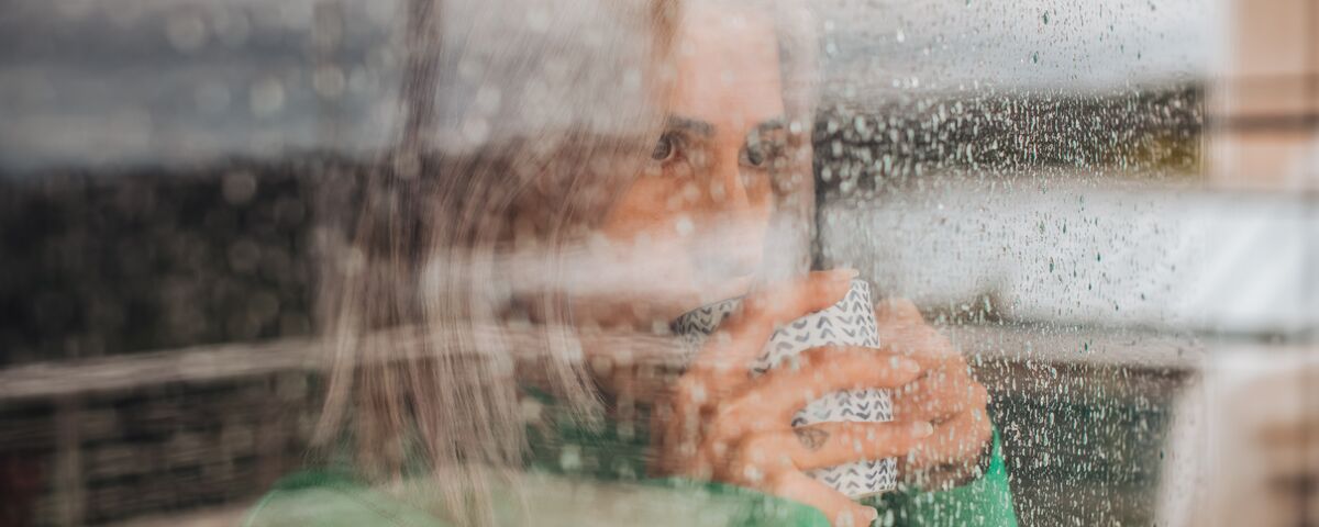 Woman drinking coffee behind glass window on a rainy day.