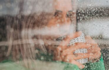 Woman drinking coffee behind glass window on a rainy day.